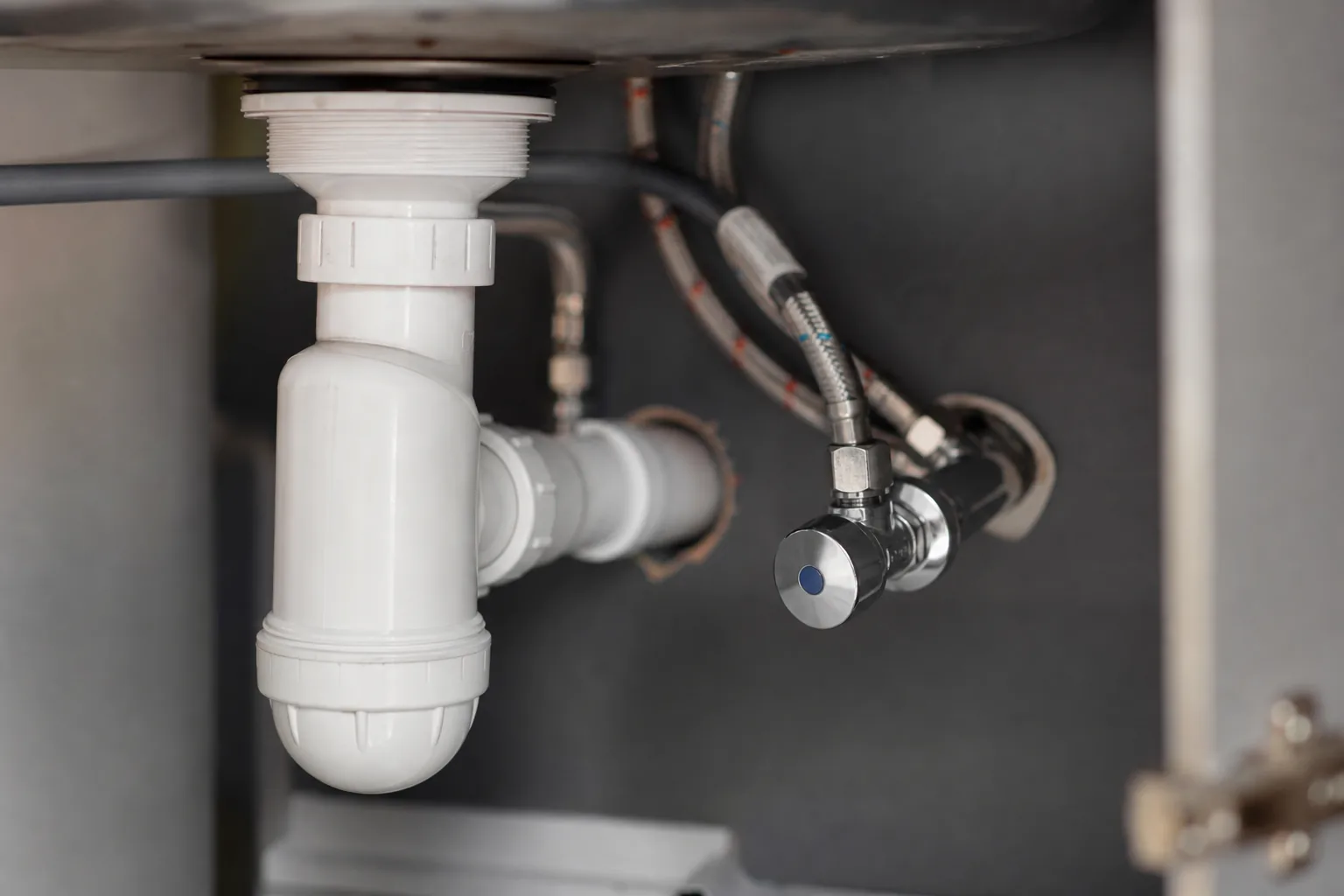 Siphon et flexibles raccordés sous un évier, robinets d’arrêt visibles