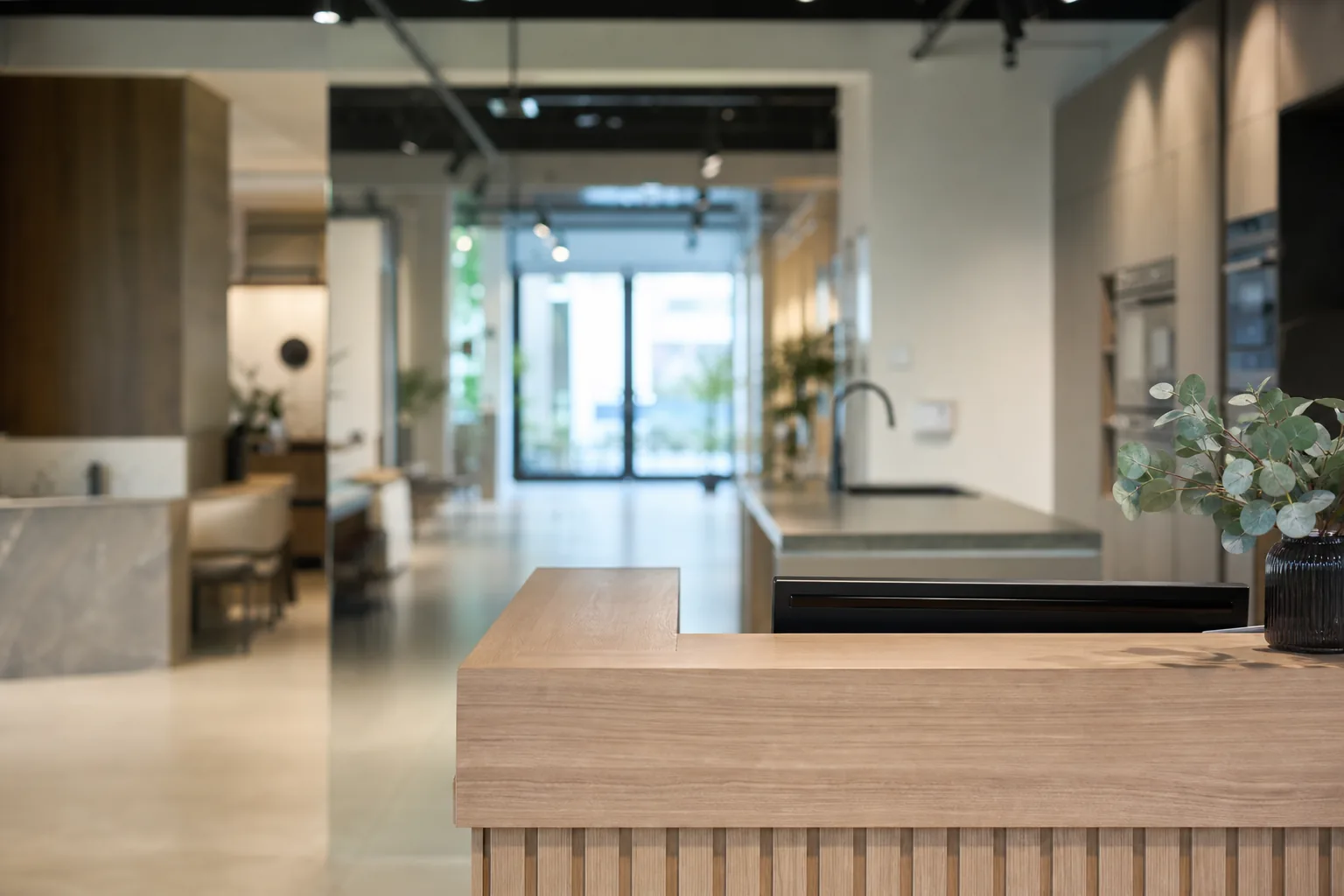 Entrée d’un showroom de cuisines vue de l’intérieur, comptoir d’accueil en bois clair au premier plan